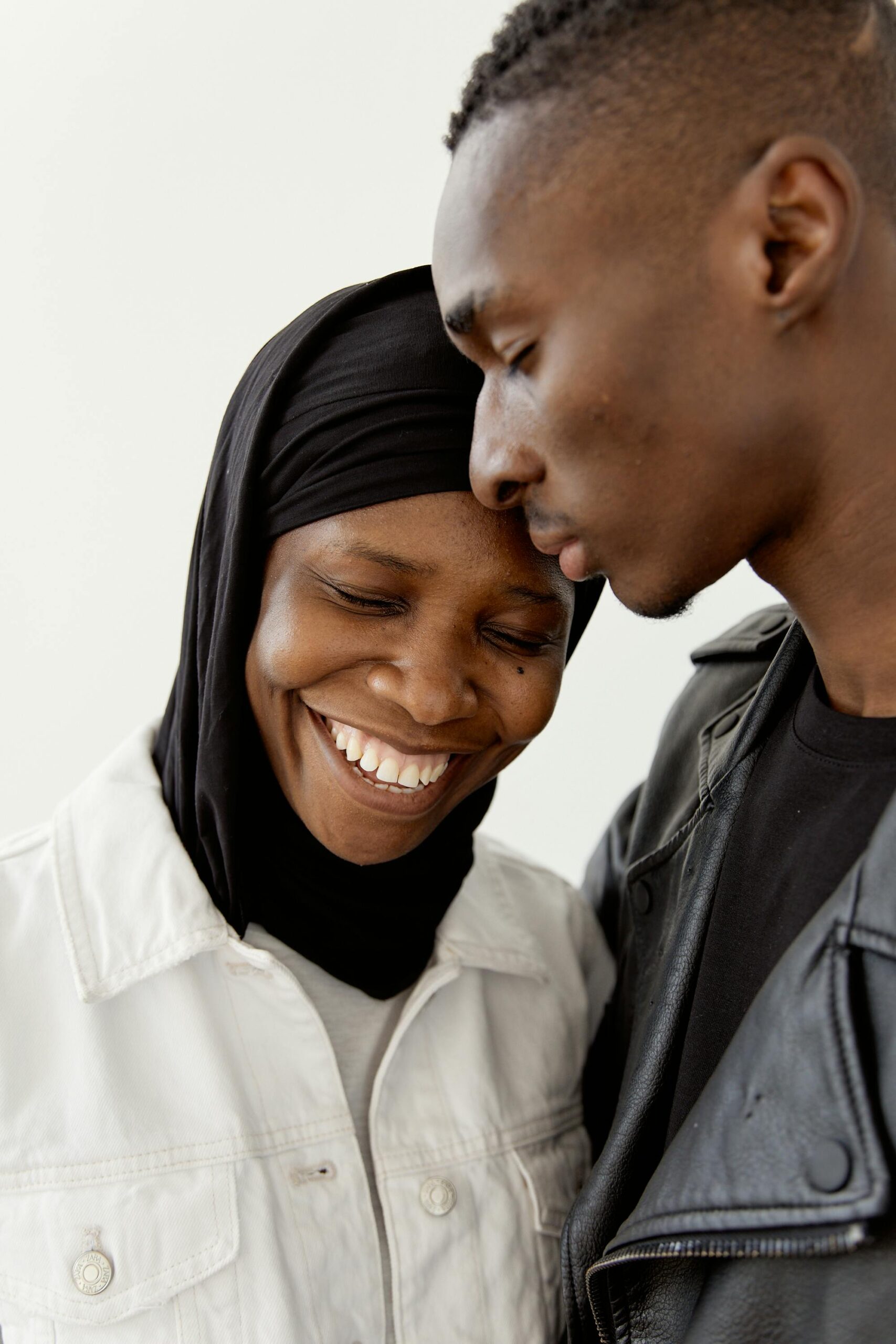 A joyful couple in black attire sharing a tender moment in a white-walled studio.