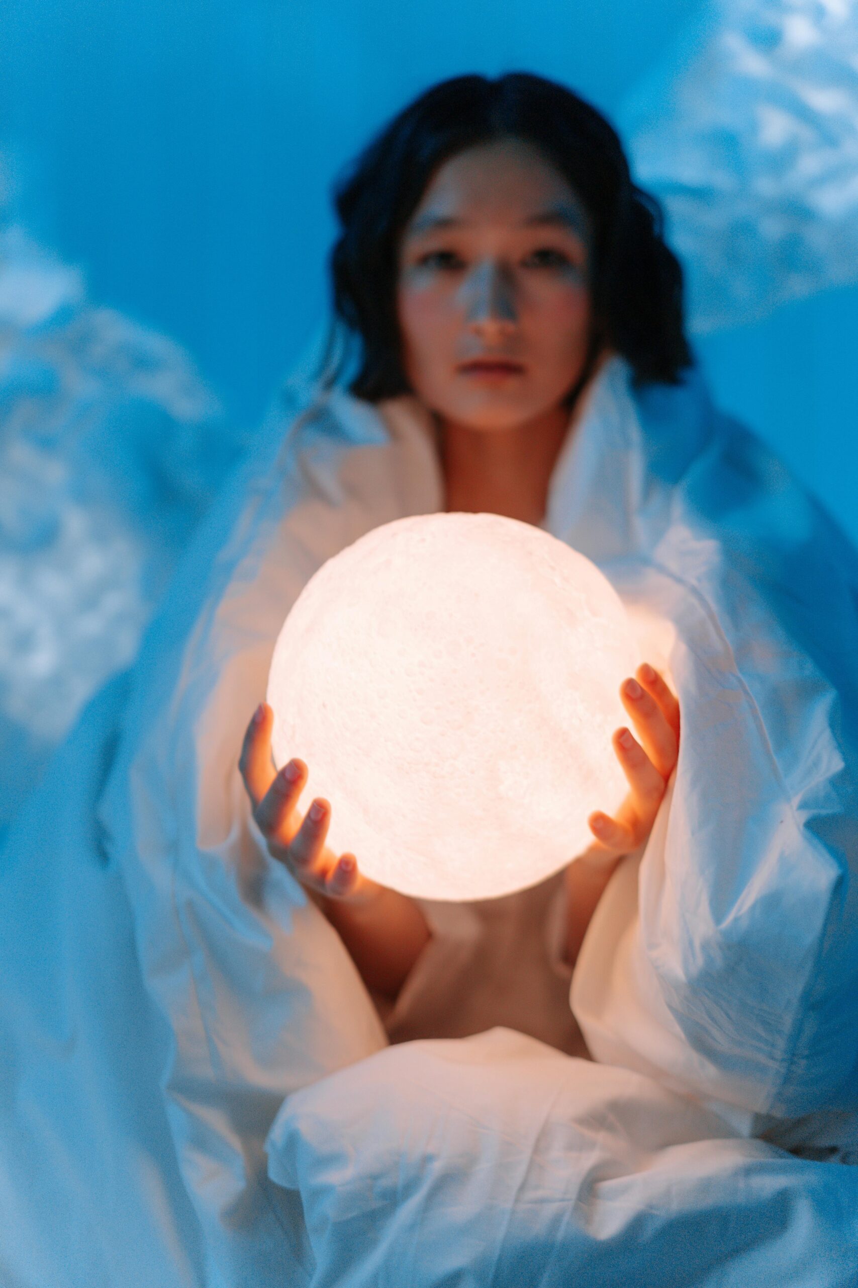 A person holds a glowing orb in a conceptual, dreamy blue setting.