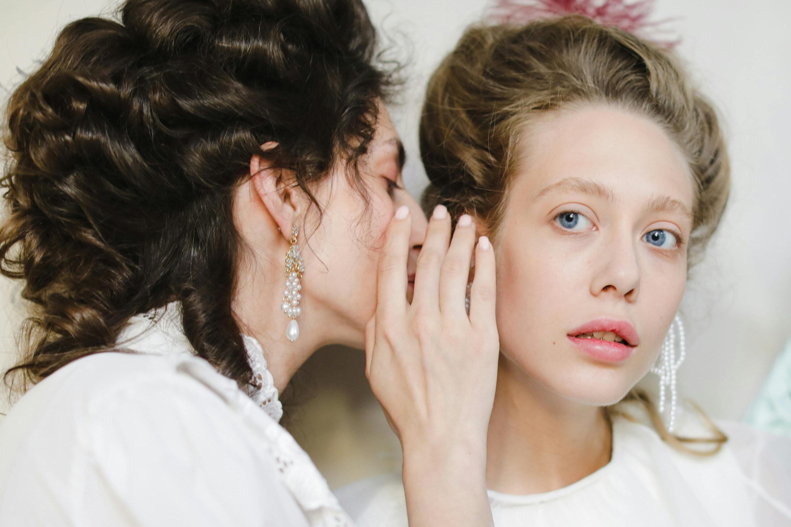 Two women dressed in 19th century fashion share a secret, showcasing elegance and friendship.